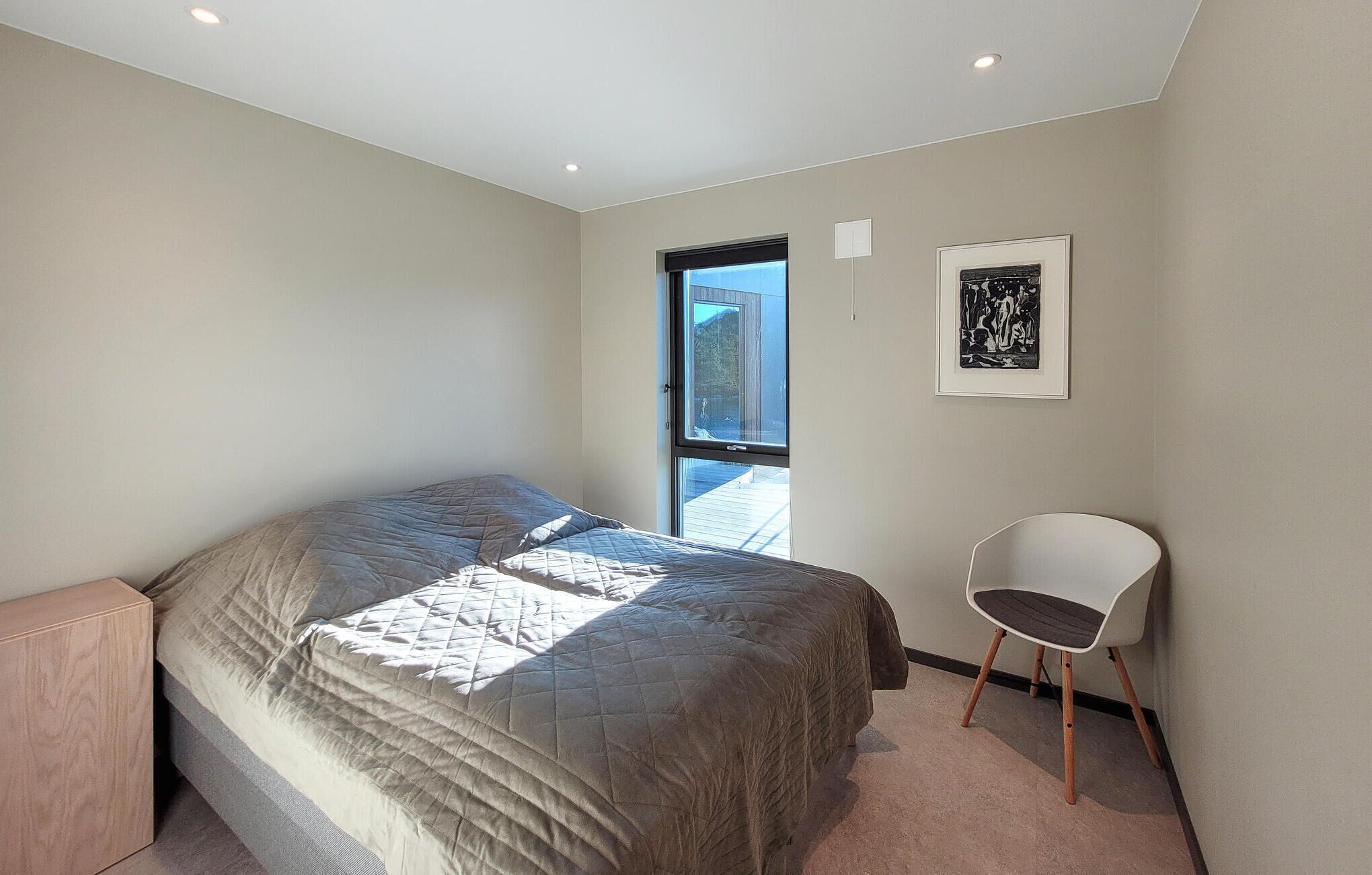 A bedroom with a bed, a chair, a window, and a framed artwork on the wall.