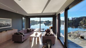 Una sala de estar moderna con un gran ventanal con vistas a un lago, un sofá, una mesa de centro y un cuadro en la pared.