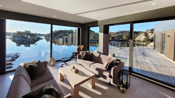 Una sala moderna con ventanas amplias, un sofá, una mesa de centro y vistas a un lago y montañas.