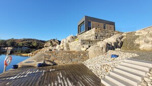 Un edificio moderno con fachada de piedra, una terraza de madera y una escalera de piedra que lleva a un muelle.
