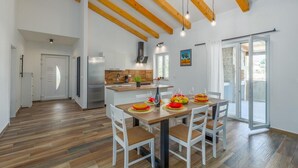 A spacious kitchen with wooden beams, a central island, and a dining area with a table set for four. - Pet friendly home in Debeljuhi (Debeljuhi)