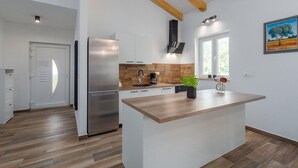 A modern kitchen with a central island, stainless steel appliances, wooden flooring, and a window providing natural light. - Pet friendly home in Debeljuhi (Debeljuhi)