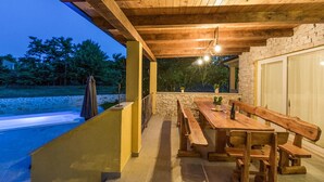 An outdoor patio with a wooden table and benches, a stone wall, and a view of a swimming pool. - Pet friendly home in Debeljuhi (Debeljuhi)