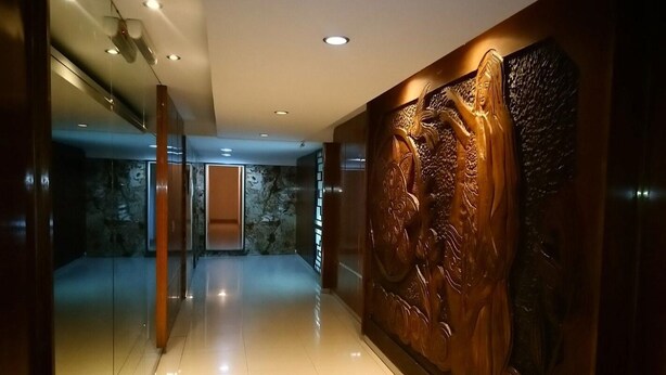 Un pasillo con suelo pulido, una pared con un relieve escultórico y una puerta con un panel de vidrio.