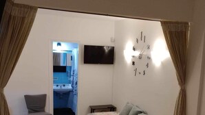 Un dormitorio con cama, una silla, un televisor y un reloj en la pared.