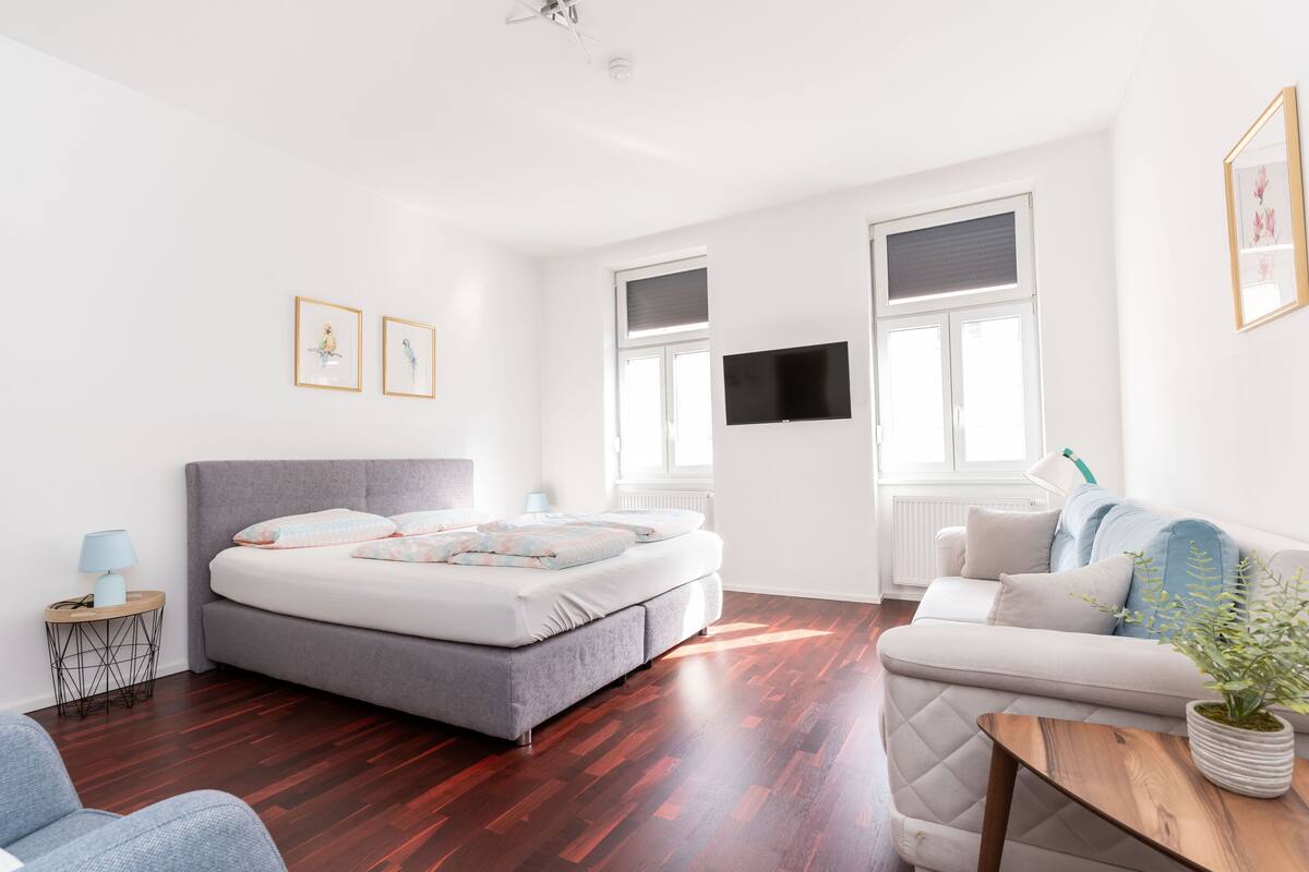 Ein modernes Schlafzimmer mit einem grauen Sofa, einem Holztisch und einem Bett mit grauem Kopfteil.