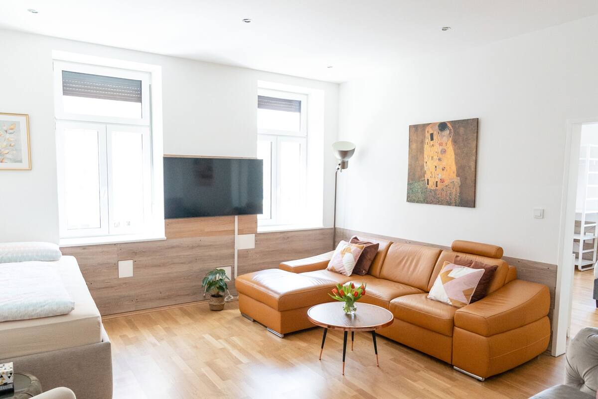 Ein modernes Wohnzimmer mit einem Ecksofa, einem grauen Sessel und einem kleinen Tisch mit einer Vase.
