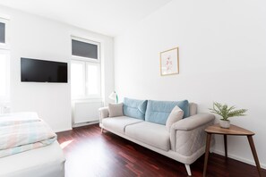 A modern living room with a white sofa, a small wooden side table with a plant, and a mounted TV.