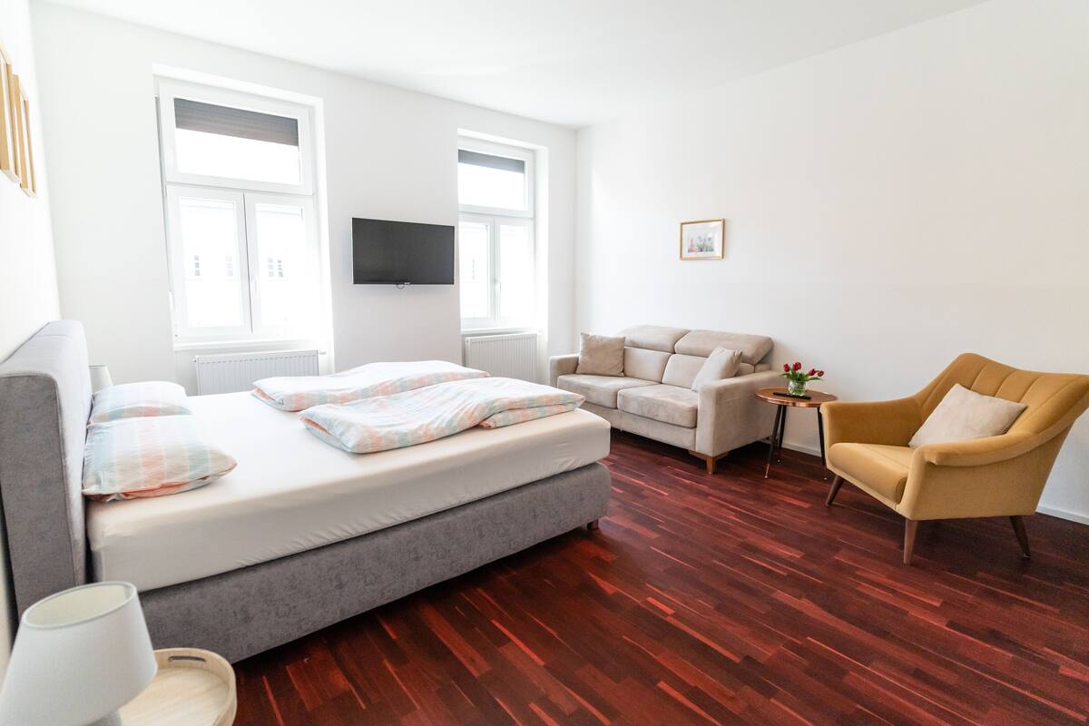 Ein modernes Schlafzimmer mit einem Bett, einer Couch, einem Sessel und einem kleinen Tisch.