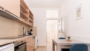 A modern kitchen with built-in appliances, a dining area with a wooden table and blue chairs, and a view of the hallway leading to a door. - Comfortable Apartments Vienna 1100  (Vienna)