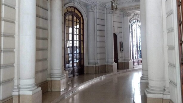A grand hallway with white columns, large arched doorways, and a chandelier.