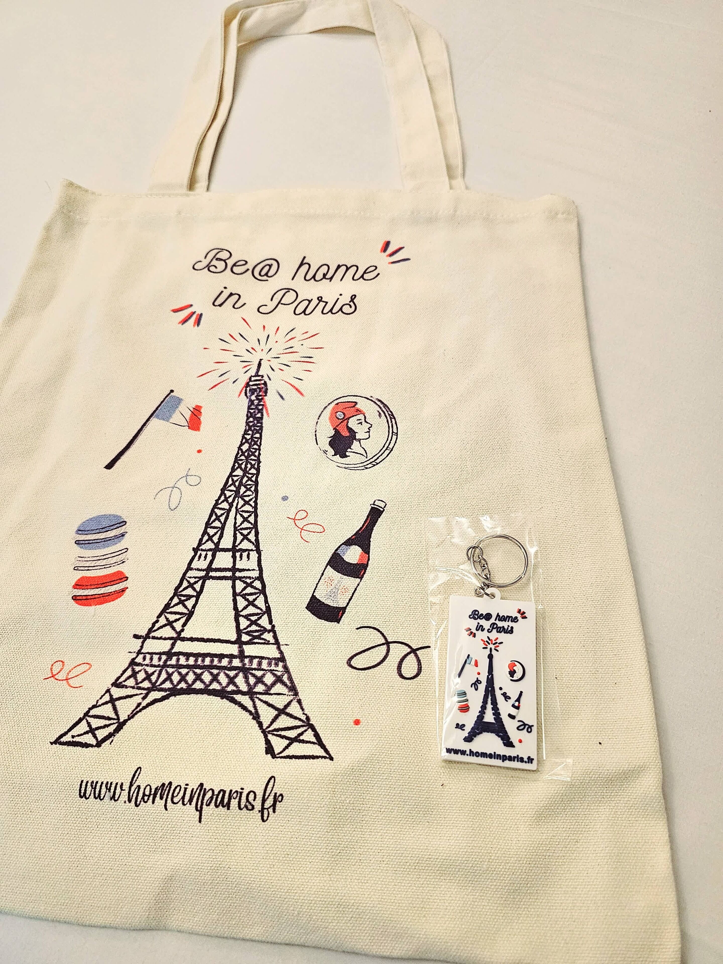 Een tas met illustraties van de Eiffeltoren en de Franse vlag, en de tekst 'Be @ home in Paris' met een website URL.