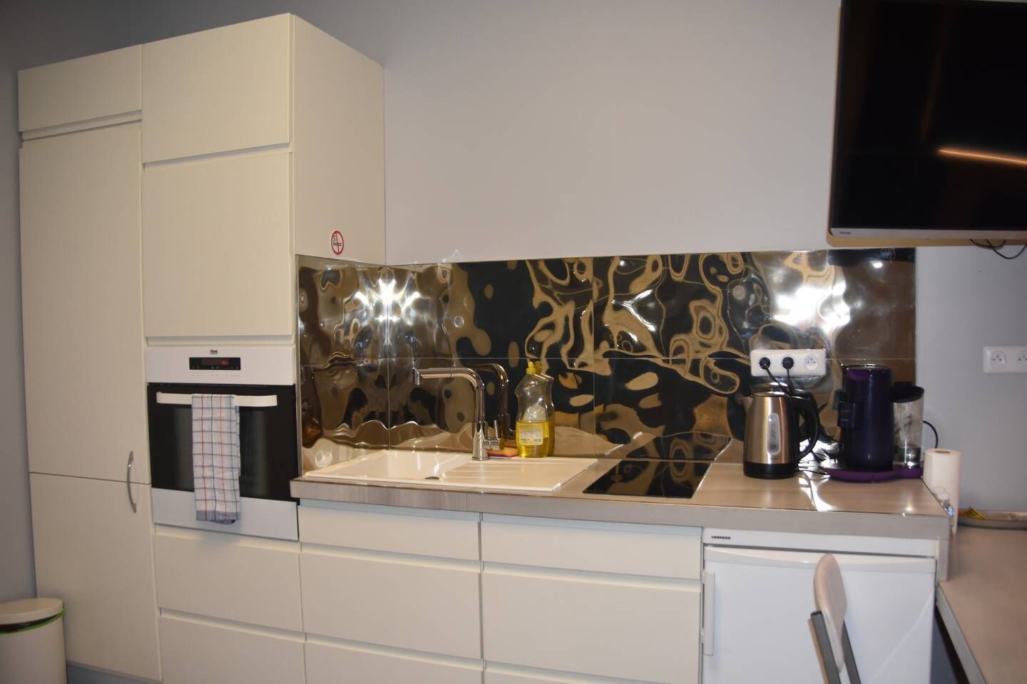 Een compacte keuken met een modern design, voorzien van een RVS-gootsteen, een inbouwoven en een magnetron.