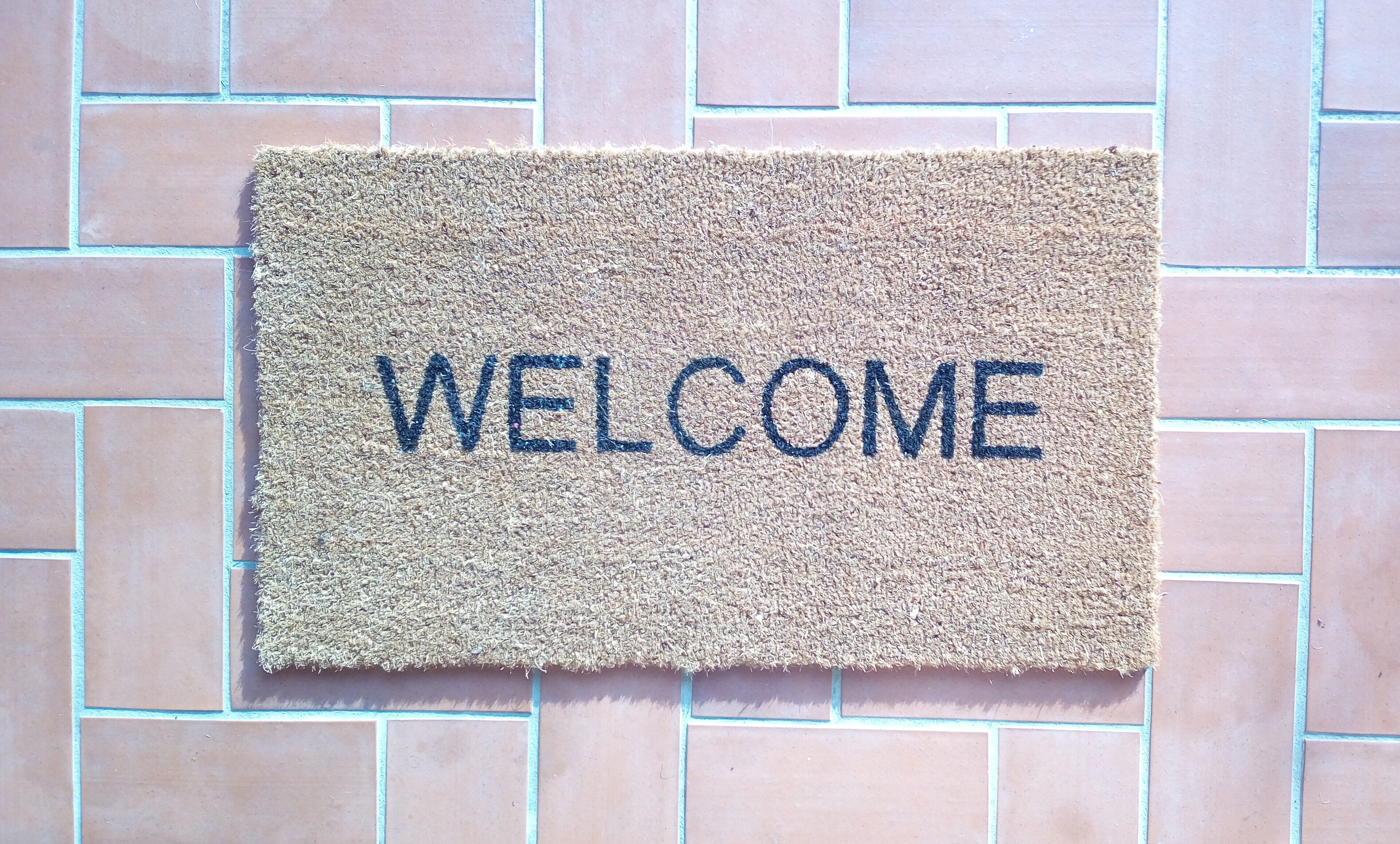A welcome mat with the word "WELCOME" on a tiled wall.