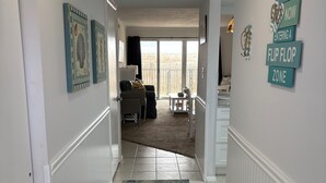 Un couloir avec un tapis à motifs, un coin repas avec une table et des chaises, et une vue sur un espace extérieur, visible à travers une porte vitrée.