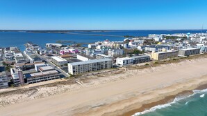 Vue aérienne d’une ville côtière avec une zone hôtelière en bord de mer, comprenant des bâtiments, une jetée et une plage de sable.