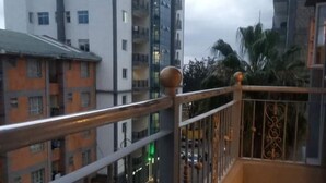 A balcony with a metal railing and a view of a parking area with cars and buildings in the background. - Lux Suites Neema court Apartments (Nairobi)