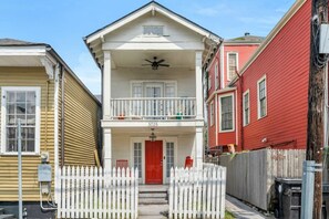 A two-story house with a red front door, white picket fence, and a balcony with railings. - Irish Channel Apt w/ Balcony | Walk to Magazine St (New Orleans)