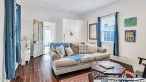 A living room with a beige sofa, a coffee table, and a patterned rug. - Irish Channel Apt w/ Balcony | Walk to Magazine St (New Orleans)