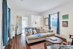 A living room with a beige sofa, a coffee table, and a patterned rug. - Irish Channel Apt w/ Balcony | Walk to Magazine St (New Orleans)