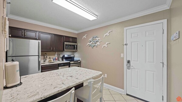 A kitchen with dark cabinets, a refrigerator, a microwave, a stove, and a sink.
