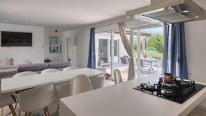 A modern kitchen with a gas stove, a dining area with a white table and chairs, and a large sliding glass door leading to an outdoor patio. - Amazing home in Pazin (Pazin)