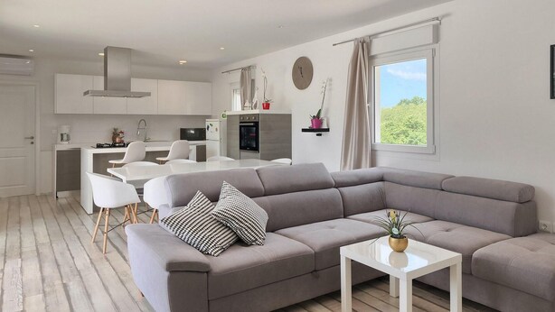 A modern living room with a grey sectional sofa, a small white coffee table, and a dining area with white chairs. - Amazing home in Pazin (Pazin)