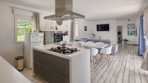 A modern kitchen with a central island, a built-in oven, and a gas stove. There is a dining area with a gray sofa and white chairs. - Amazing home in Pazin (Pazin)