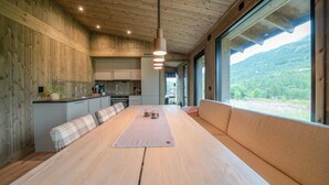 A modern kitchen with wooden walls, a dining area with a long table and benches, and large windows offering a view of the outdoors. - 3 bedroom nice home in Vøringsfoss (Vøringsfoss)