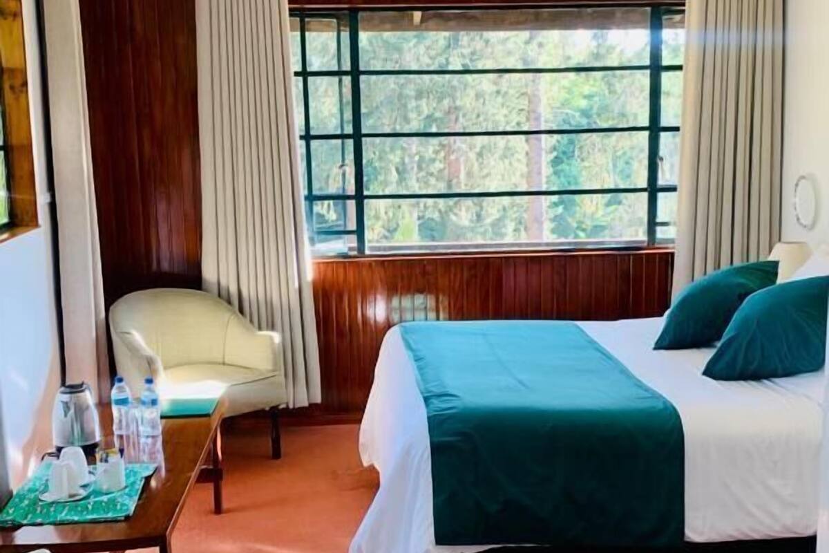 A hotel room with a bed, a chair, a table with water bottles, and a window with curtains.