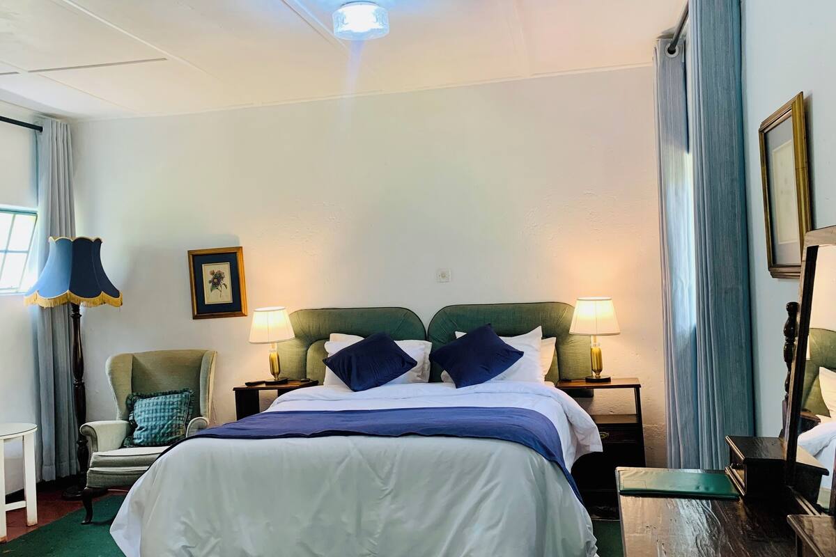 A hotel room with a bed, two bedside tables with lamps, a chair, a small table, and a mirror.