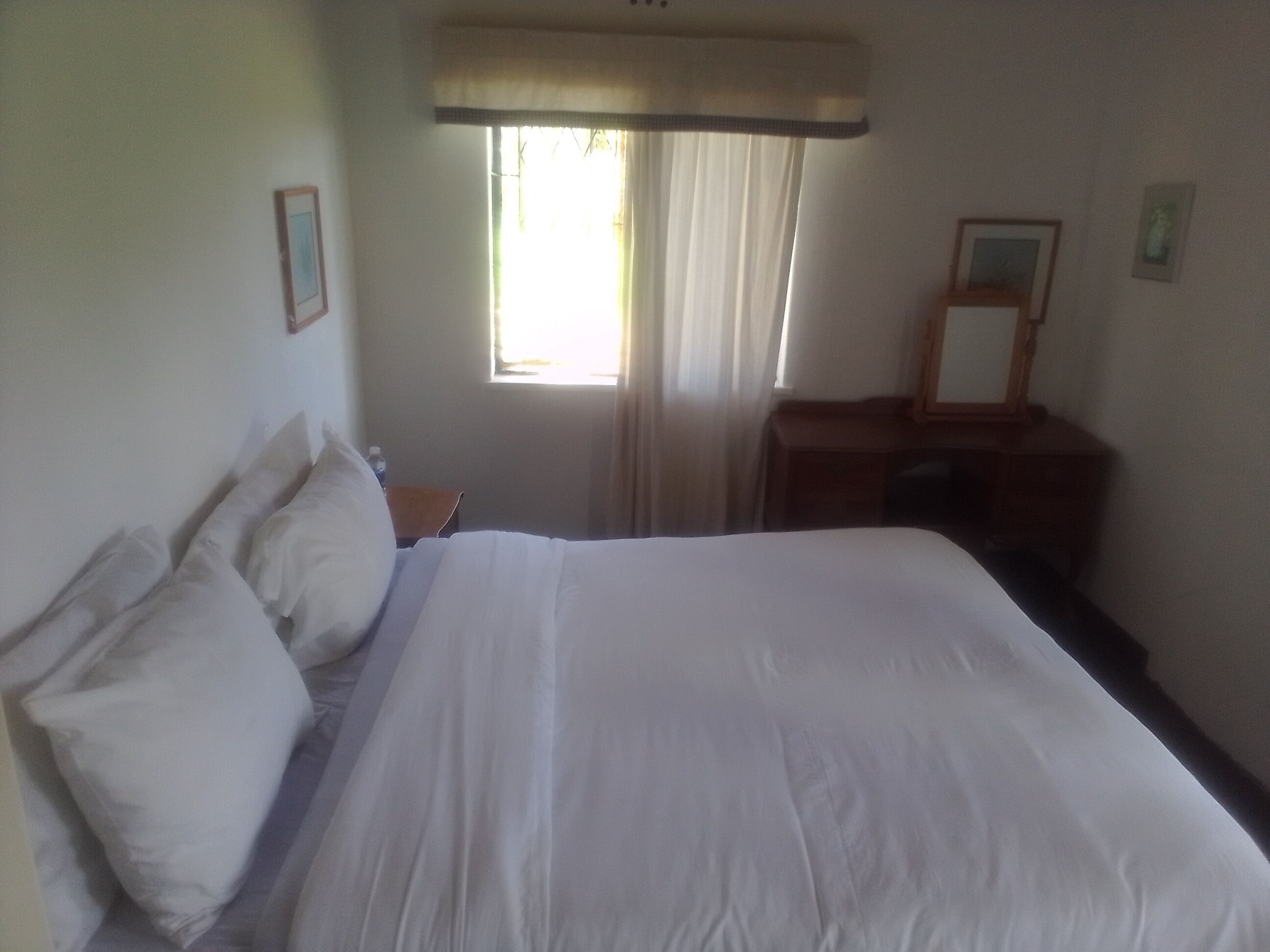 Ein Hotelzimmer mit einem großen Bett, einem Nachttisch, einem Spiegel und einem Fenster mit Vorhängen.