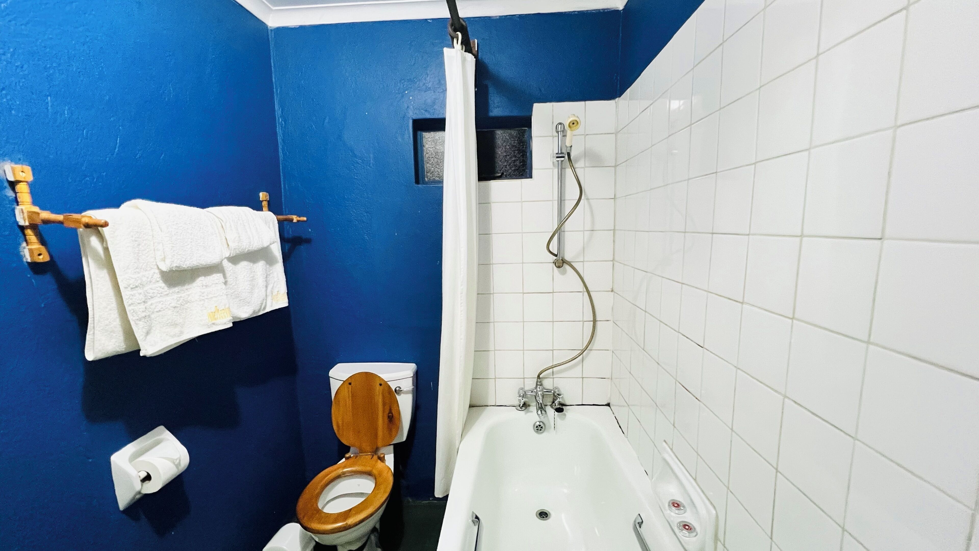 A bathroom with a blue wall, a white bathtub, and a wooden toilet.