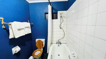 A bathroom with a blue wall, a white bathtub, and a wooden toilet.