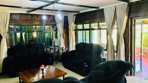 A room with two dark-colored sofas, a wooden coffee table with a vase of flowers, and a large window with curtains.