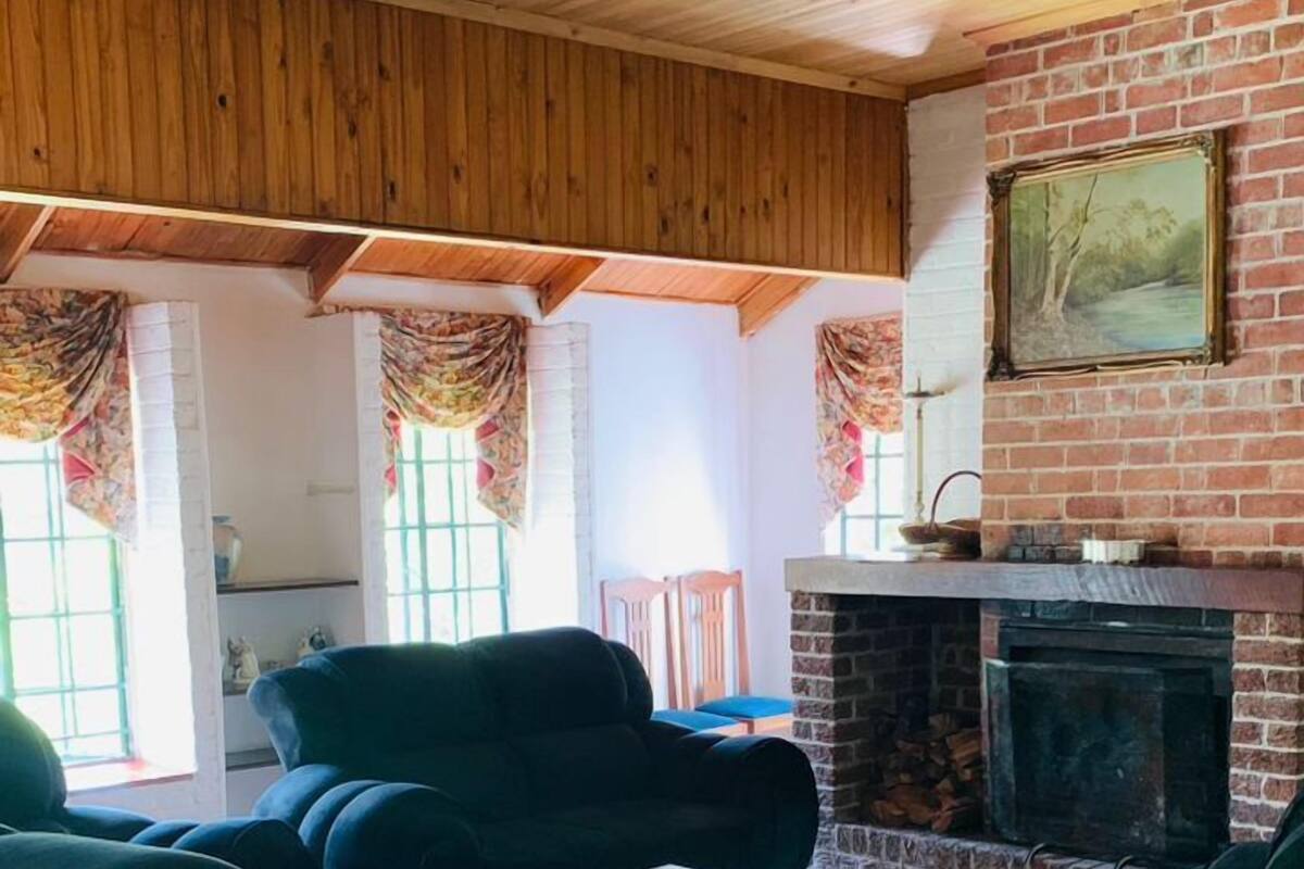 A cozy living room with a brick fireplace, wooden ceiling, and large green armchairs.