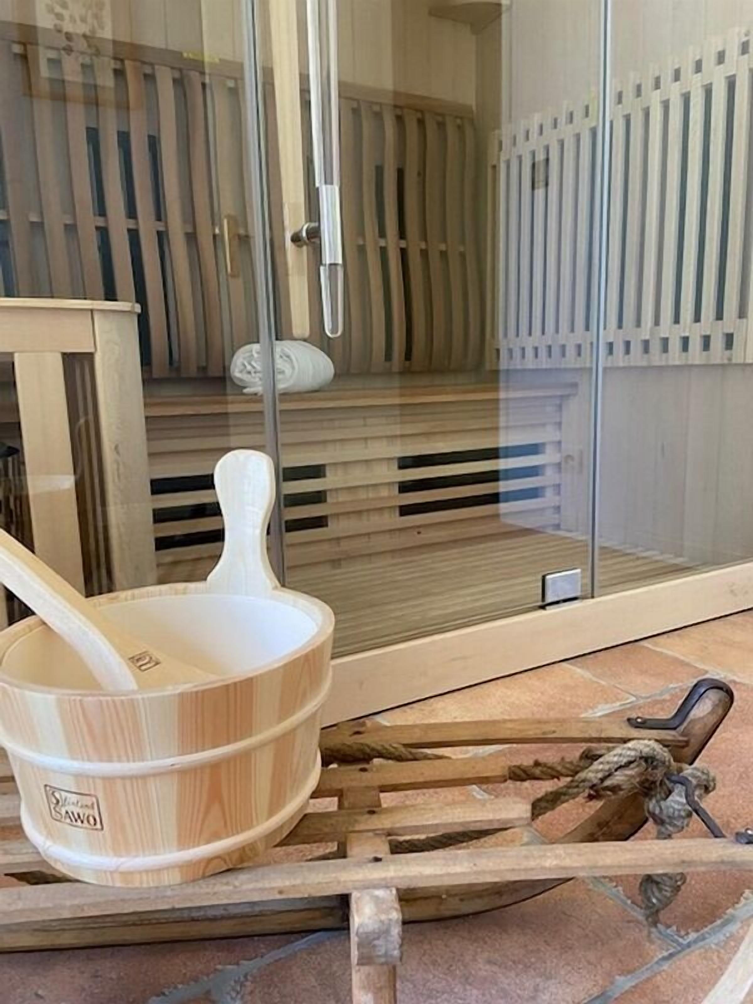 A sauna room with a wooden bench, a wooden bucket, and a sauna brush.