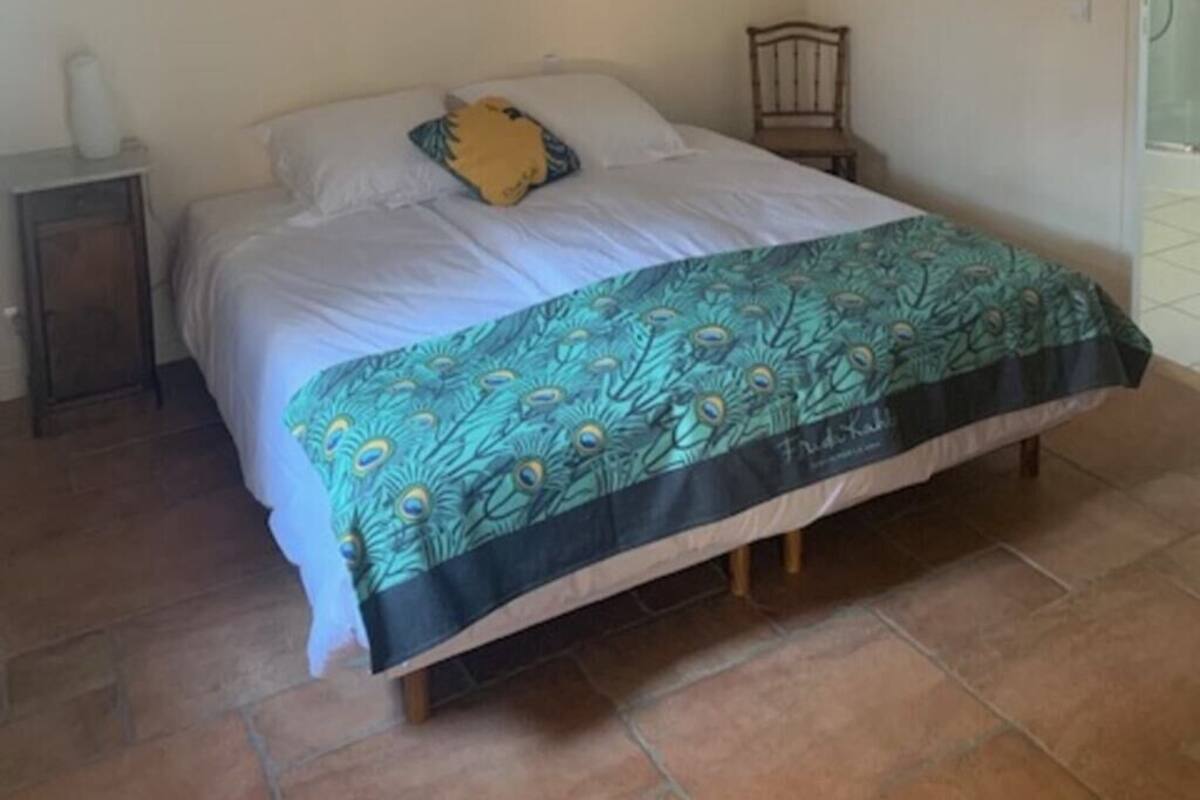 A bedroom with a bed, a nightstand, a wall-mounted light, and a door.