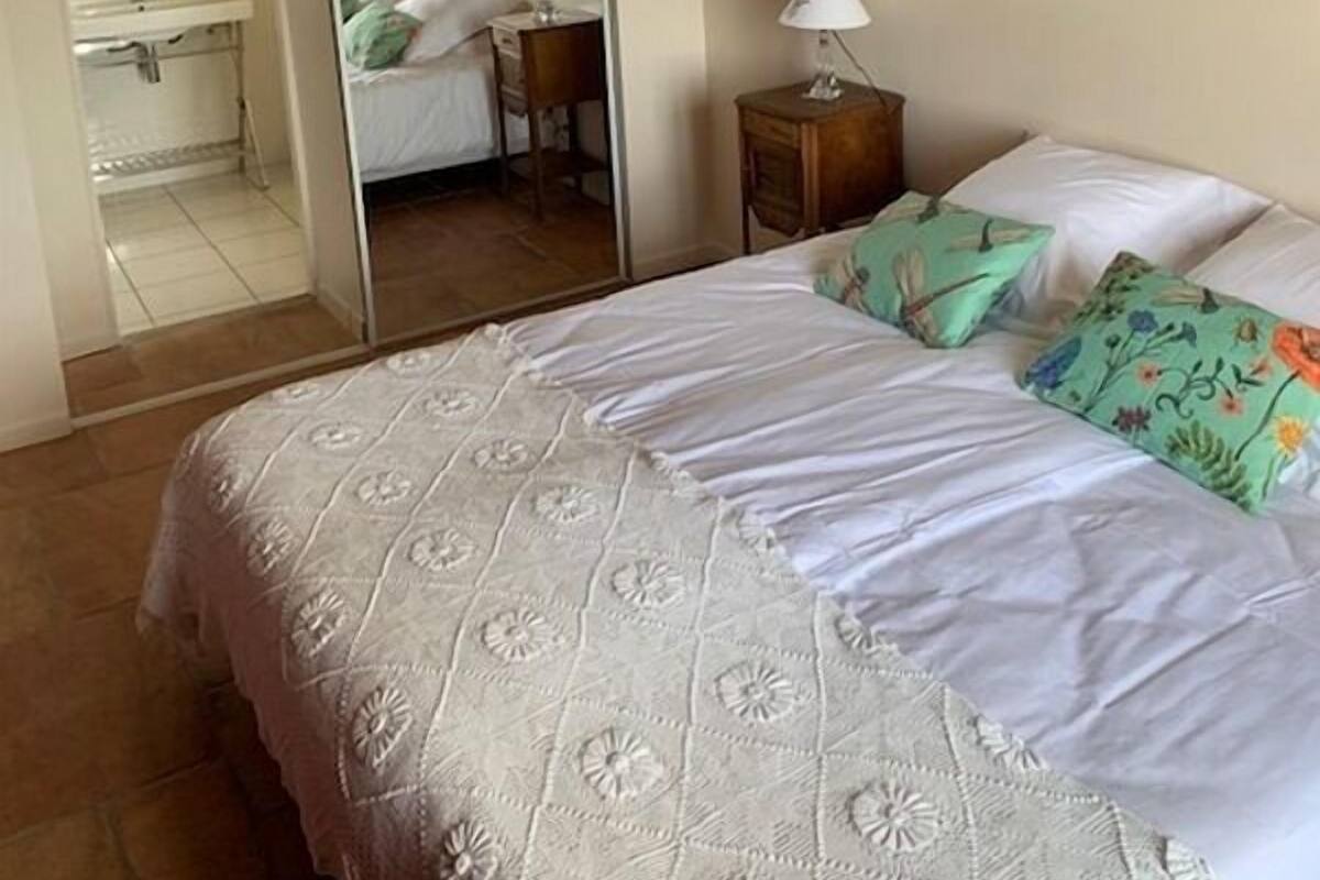 A bedroom with a large bed, a mirror, a nightstand, and a bathroom visible through the mirror.
