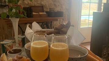 A breakfast table with fruit, cheese, and drinks, a vase with flowers, and a rustic stone wall.