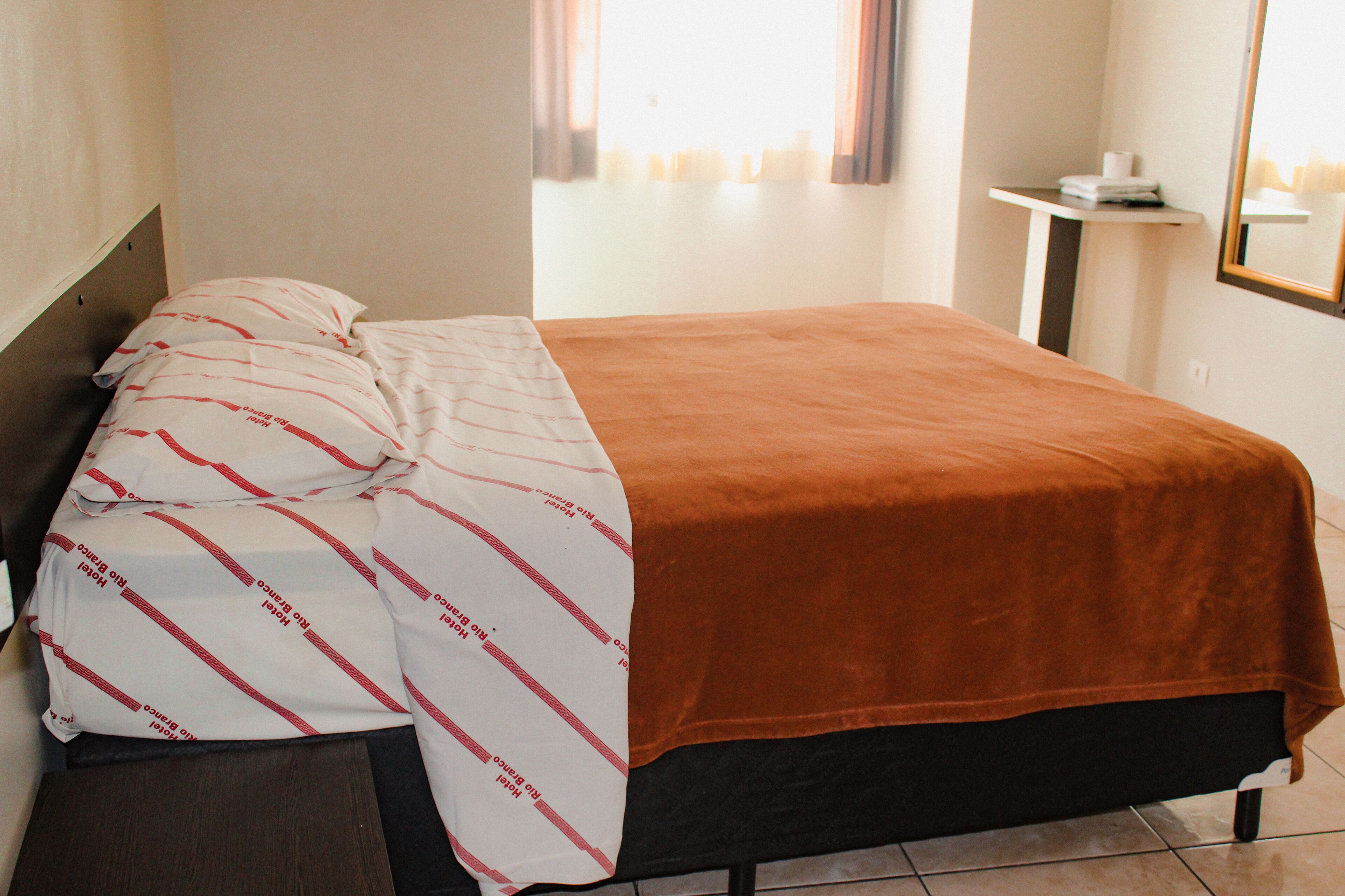 Une chambre d’hôtel avec un lit, une table de chevet, un miroir et une fenêtre avec des rideaux.