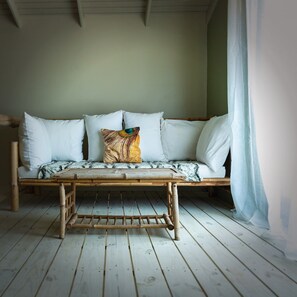 Una habitación con piso de madera, estructura de cama de bambú y una cama blanca con muchos almohadones.