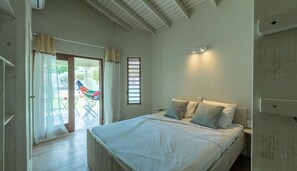 A bedroom with a bed, a nightstand, a window with blinds, and a view of the outside. - Hofi Paradise @ Sunset Heights | Private Pool (Sunset Heights)