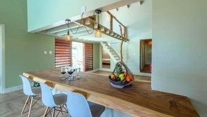 Eine Küche mit einer Holzeinrichtung, weißen Stühlen, einer Obstschale und einer Treppe.