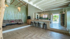 Amplia sala de estar con piso de espiga, un sofá, una mesa de centro de madera y una cocina con un ventanal grande.