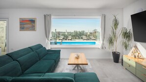 A modern living room with a green sofa, a wooden coffee table, and a view of a swimming pool and outdoor area. - Beach front home in Babici (Babici)
