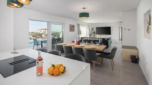A modern kitchen with a dining area, a TV mounted on the wall, and a view of the outside. - Beach front home in Babici (Babici)
