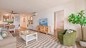 A living room with a sofa, coffee table, and a television on a wooden cabinet. - Top Floor Condo- Ocean Views w Pool Steps to Beach (Wailuku)