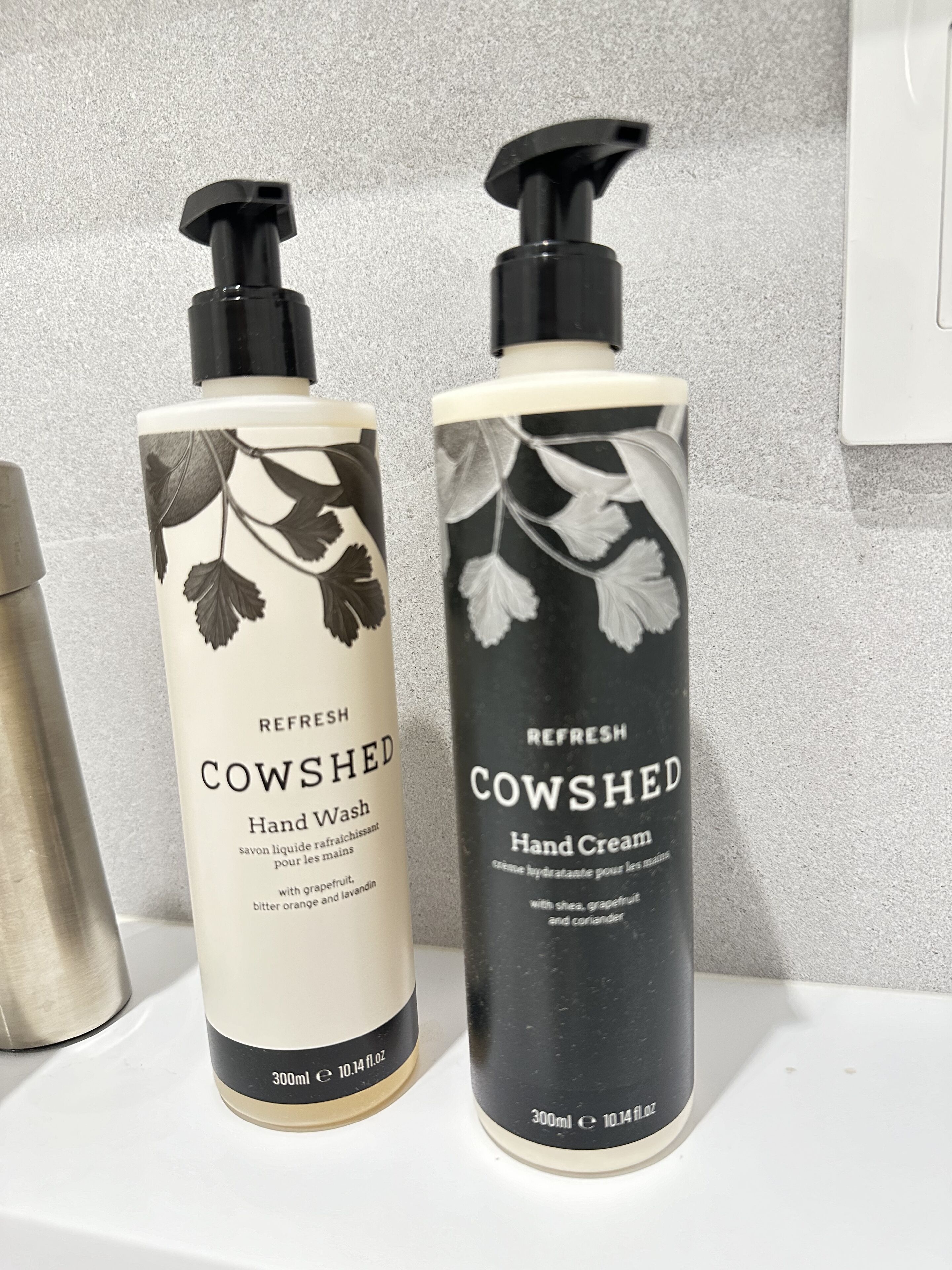 To flasker COWSHED håndvask og håndcreme på en hvid overflade.