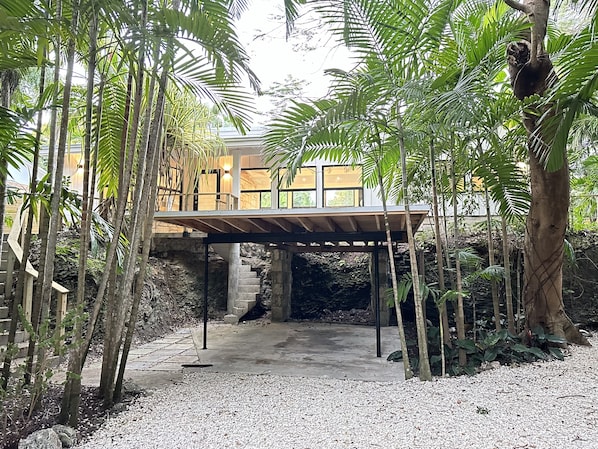 A modern house with a covered patio, surrounded by lush greenery and a stone staircase leading to a second level.
